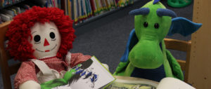 Raggedy Ann doll and a stuffed dragon at a table reading books